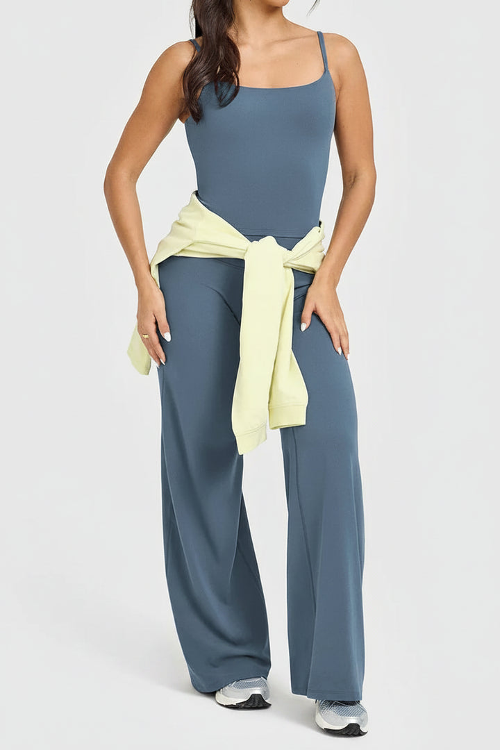 Woman wearing a blue jumpsuit with a yellow wrap, standing against a white background.